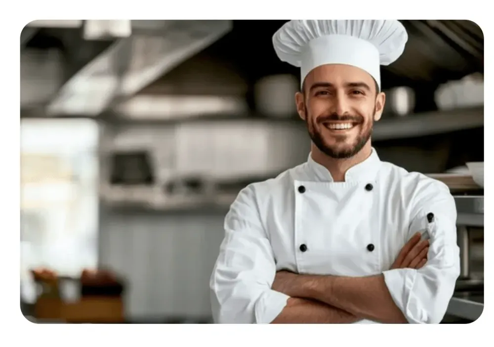 Cuisinier en tenue de chef, les bras croisés, souriant